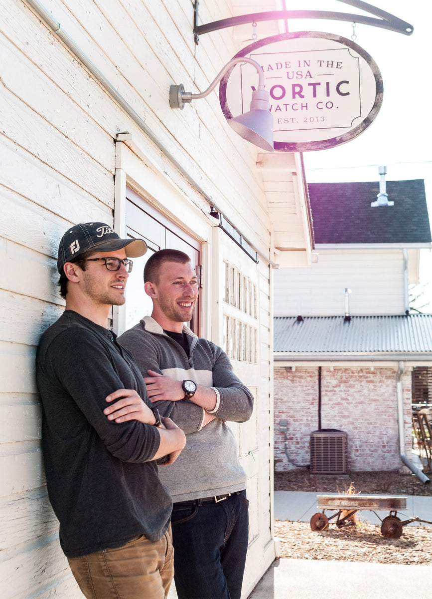 Image of two men leaning against a farmhouse building.