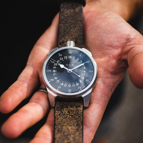 Close up of a watch being held in a hand. Stainless steel case, dark brown leather strap. 