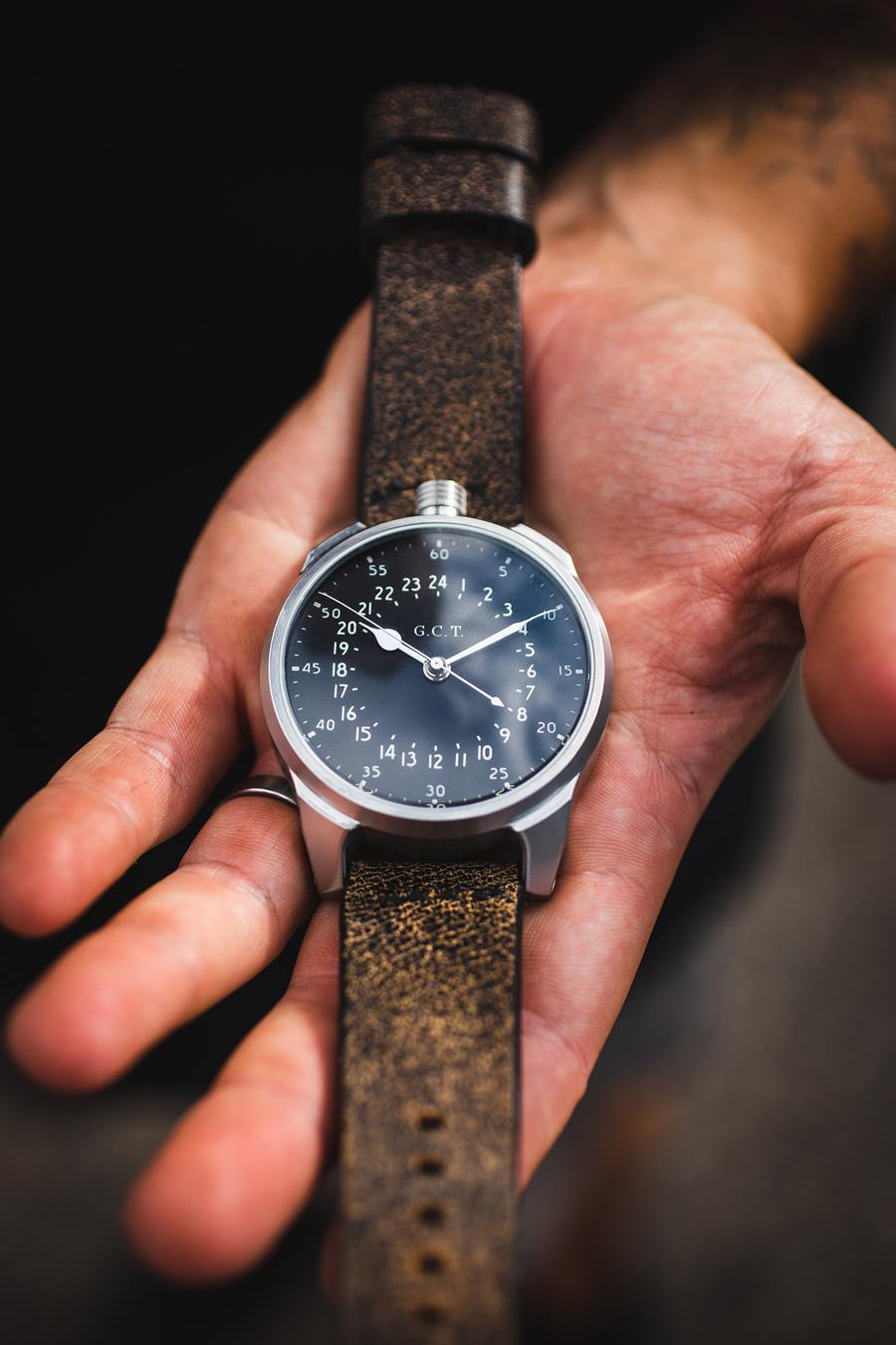 Close up of a watch being held in a hand. Stainless steel case, dark brown leather strap. 