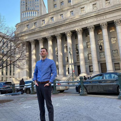 Man standing in a courtyard, blue shirt, capitol building in the background. 