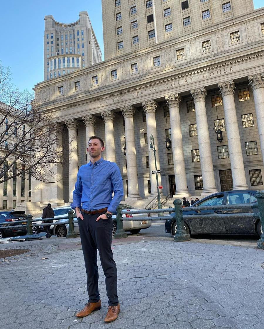 Man standing in a courtyard, blue shirt, capitol building in the background. 