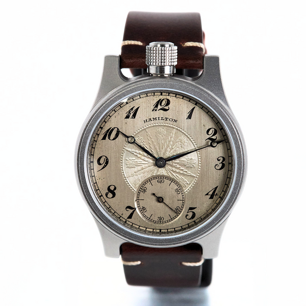 A vintage-style Hamilton watch with a silver-toned metal case, a textured beige dial with black Arabic numerals, and a dark brown leather strap, shown against a plain white background.