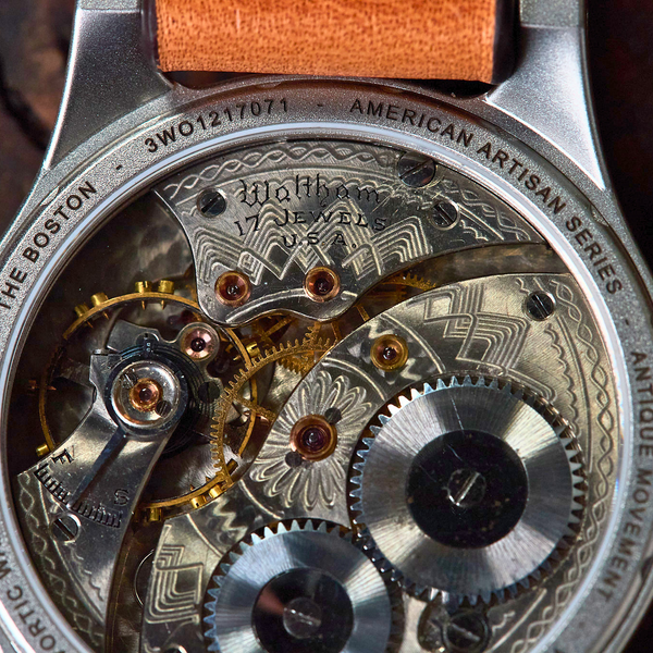 Close-up of a watch mechanism with 'American Artisan Series' branding on a wooden background.