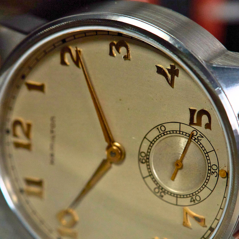 Close-up of a vintage wristwatch with a gold face and brown leather strap.