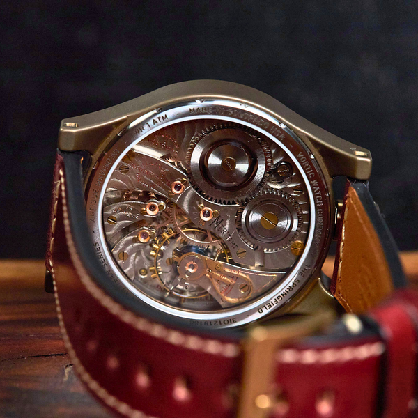 A close-up shot of a luxury watch with a transparent back, showcasing an intricate mechanical movement, resting on a dark wooden surface with a dark textured background.