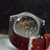 Close-up of the back of a wristwatch with a brown leather strap, showing a detailed silver-tone automatic mechanical movement through a sapphire crystal.
