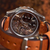 A close-up shot of a skeleton watch with a brown leather strap, showing the intricate mechanical movement through a transparent circular case.