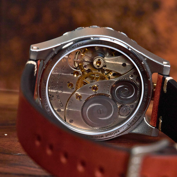 Close-up of a wristwatch with a transparent back showing a detailed mechanical movement, attached to a brown leather strap on a wooden surface.