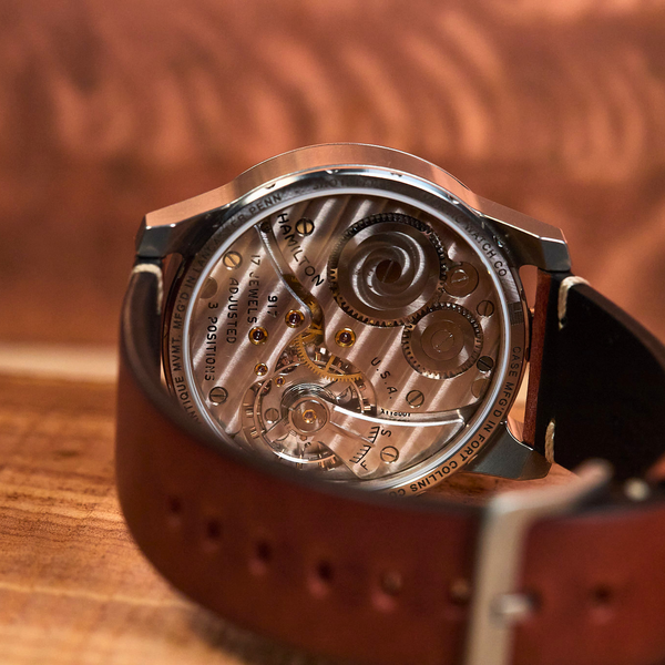 Close-up of a mechanical watch with a brown leather strap on a wooden surface