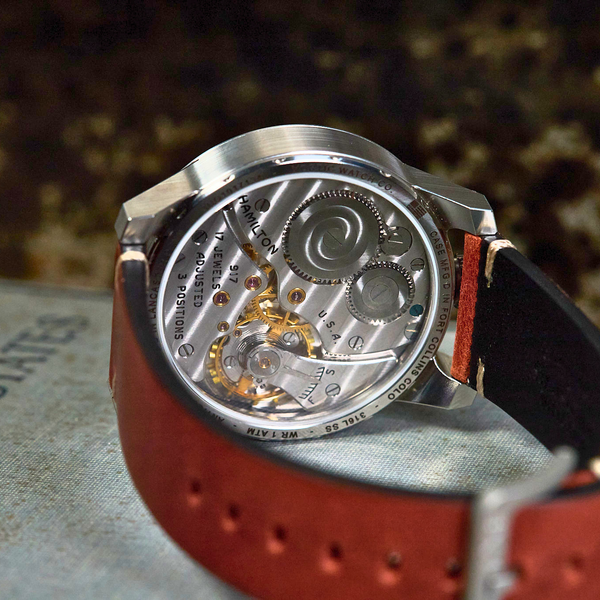 Watch with red strap and visible mechanical components on a textured surface