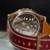 Close-up of a mechanical watch with a red leather strap on a blurred background