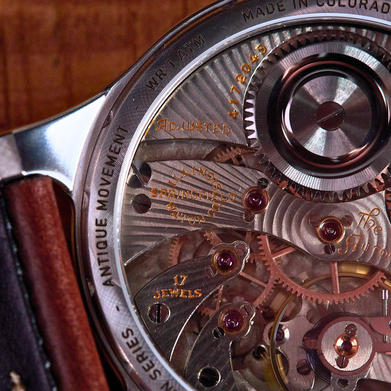 Close-up of a watch mechanism with visible brand name on a wooden surface