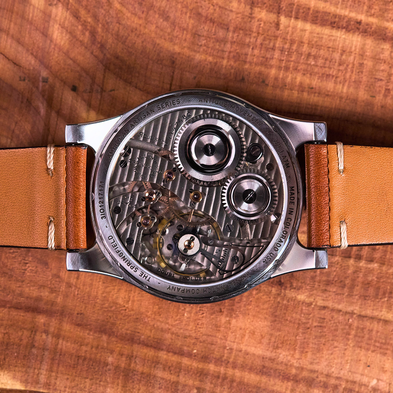 Watch with visible mechanical components on a brown leather strap against a wooden background