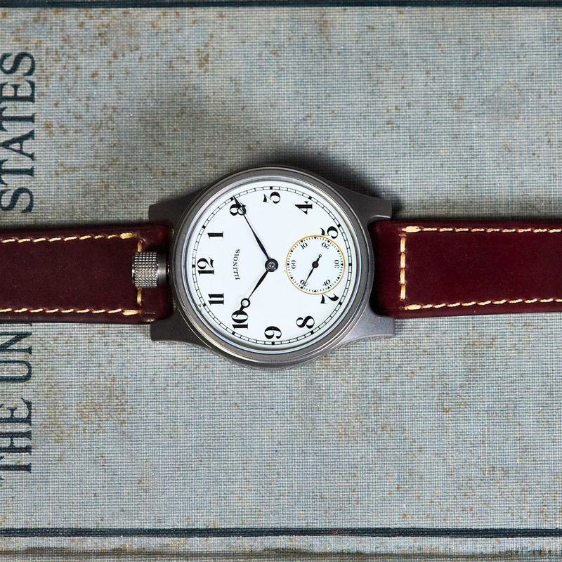 A vintage-style wristwatch with a white dial and dark brown leather strap, laid flat on top of a textured book page with printed text.