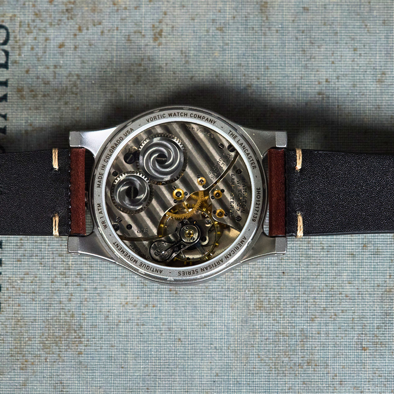 A close-up top-down view of a skeleton watch showing the intricate mechanical movement through a transparent back, attached to a black leather strap with red stitching, set against a textured blue-gray background with a vintage book page on the left.