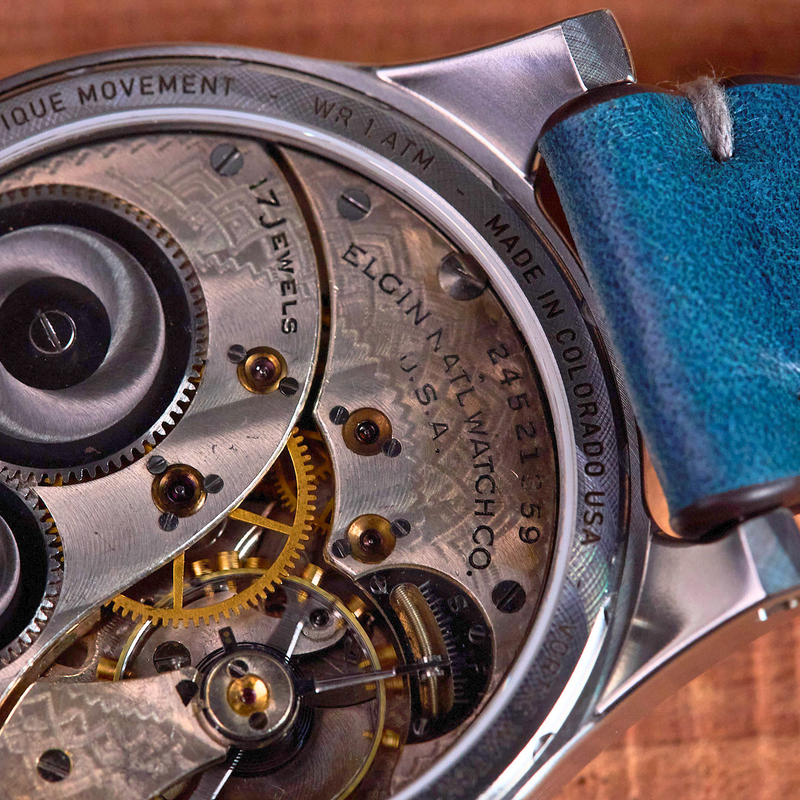 Close-up of a watch with visible mechanical components and a blue strap on a wooden surface.