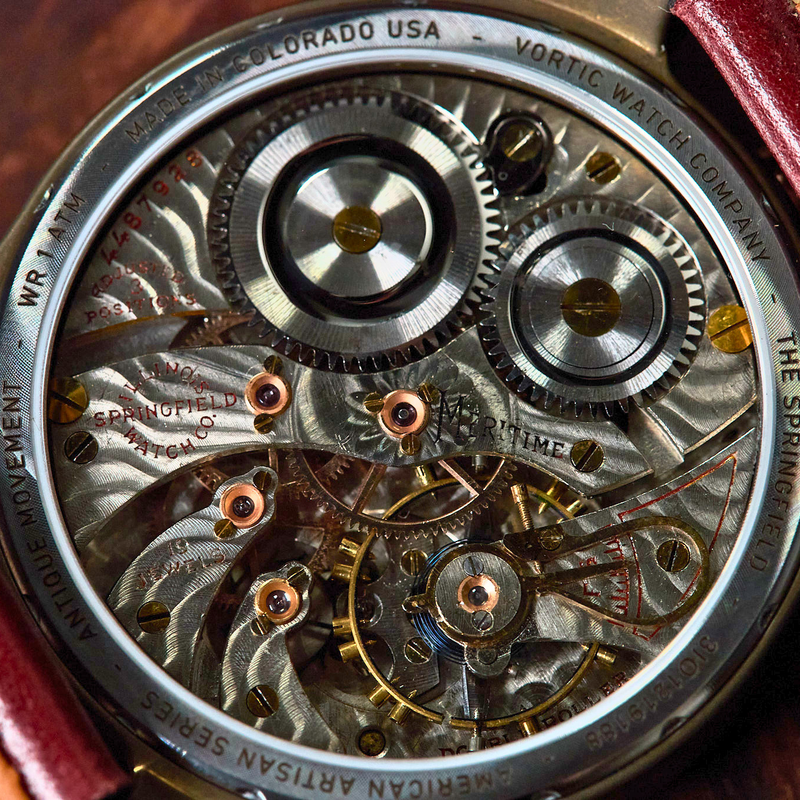 Close-up of a skeleton watch showing the intricate mechanical movement inside, with a brown leather strap visible on both sides against a dark wooden background.