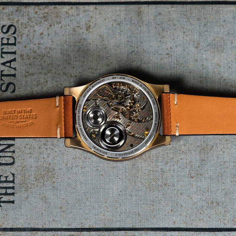 A luxury watch with a round open-back dial showing a complex mechanical movement, featuring a warm orange-brown leather strap, laid flat on a textured gray book page with black printed text.
