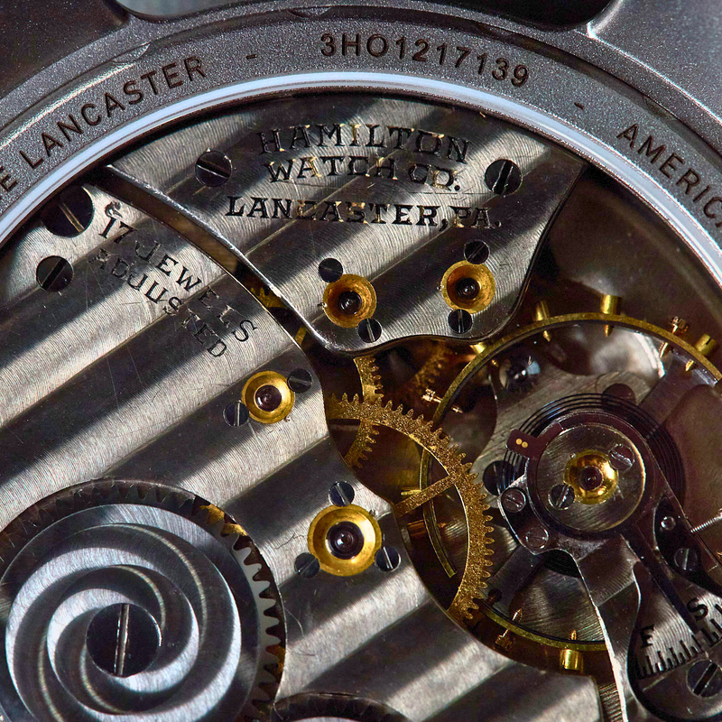 Close-up of a vintage Hamilton Watch Co. Lancaster automatic watch movement, showing silver-toned gears, gold-toned screws, and engraved text on the inner case.