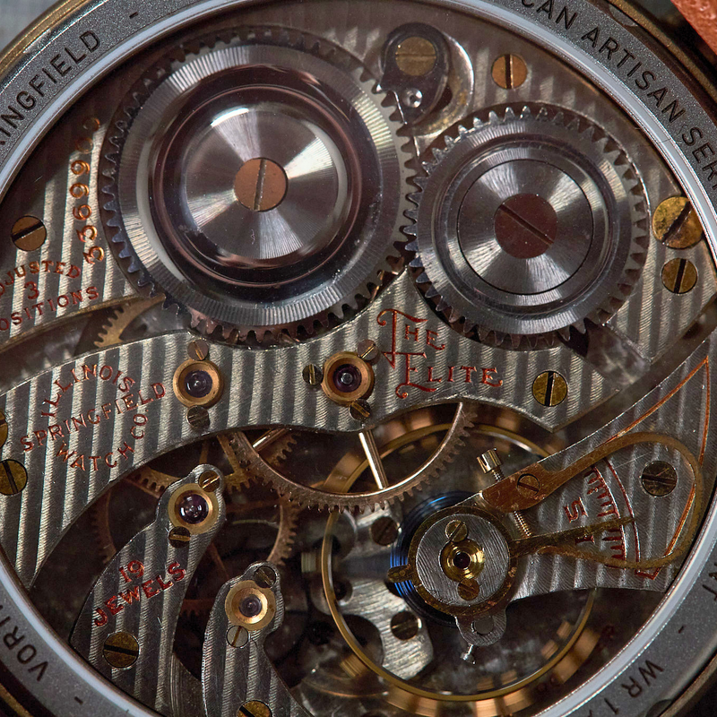 Close-up of a vintage-style automatic watch movement with exposed silver and gold-toned gears, screws, and bridges, surrounded by a brass case and brown leather strap.