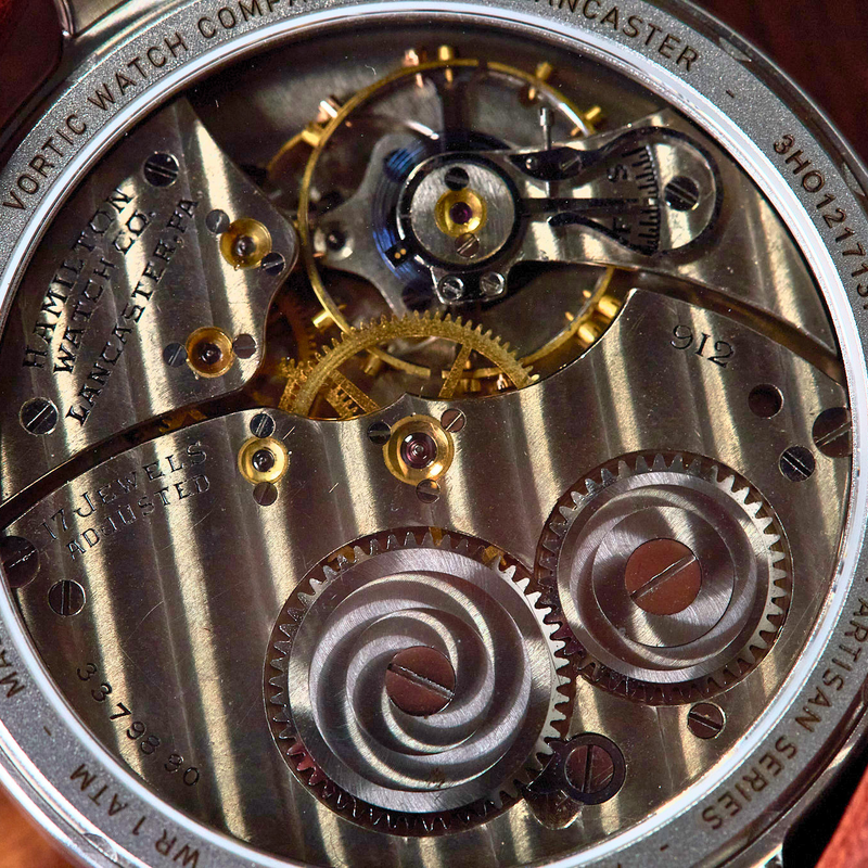 Close-up of a mechanical watch back showing the intricate gold and silver movement gears, with a brown leather strap visible on both sides.