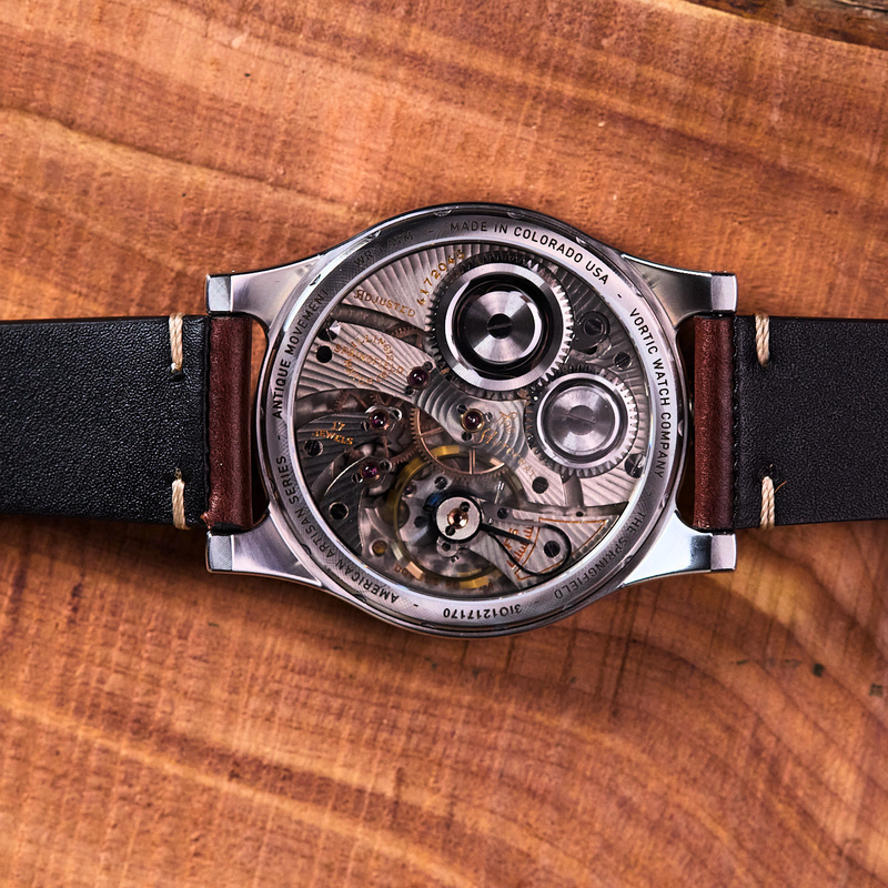 Mechanical watch with black leather strap on a wooden surface