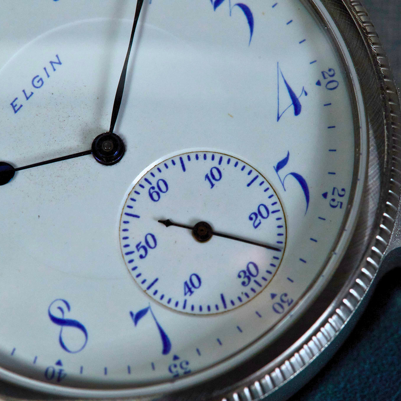 Close-up of a vintage Elgin pocket watch with blue hour markers.
