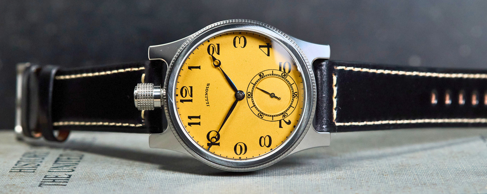 Watch with a yellow face and black strap on a book